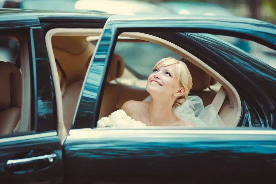 The smiling bride sits in non-stretch Black Limo car, Symbolizing Houston luxury wedding transportation services.
